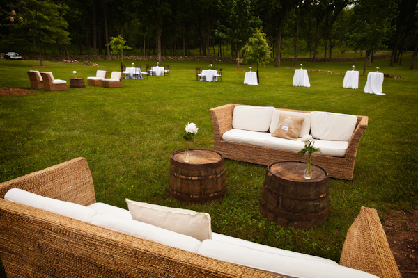 outdoor reception lounge seating area with wicker loveseats with white cushions, tables made from barrels with white rose decor - photo by Washington DC based wedding photographers Holland Photo Arts